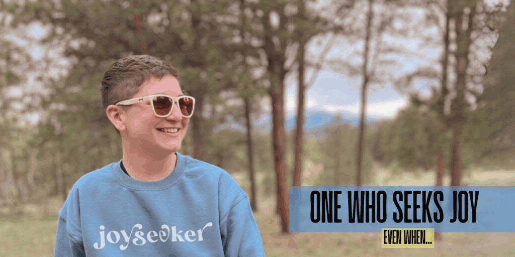 model wearing a crewneck sweatshirt in stone blue that says "joyseeker." text graphic says "one who seeks joy, even when..."